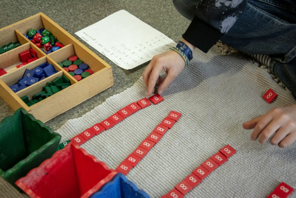 Des mains d’enfant alignent les jetons du matériel Montessori de calcul